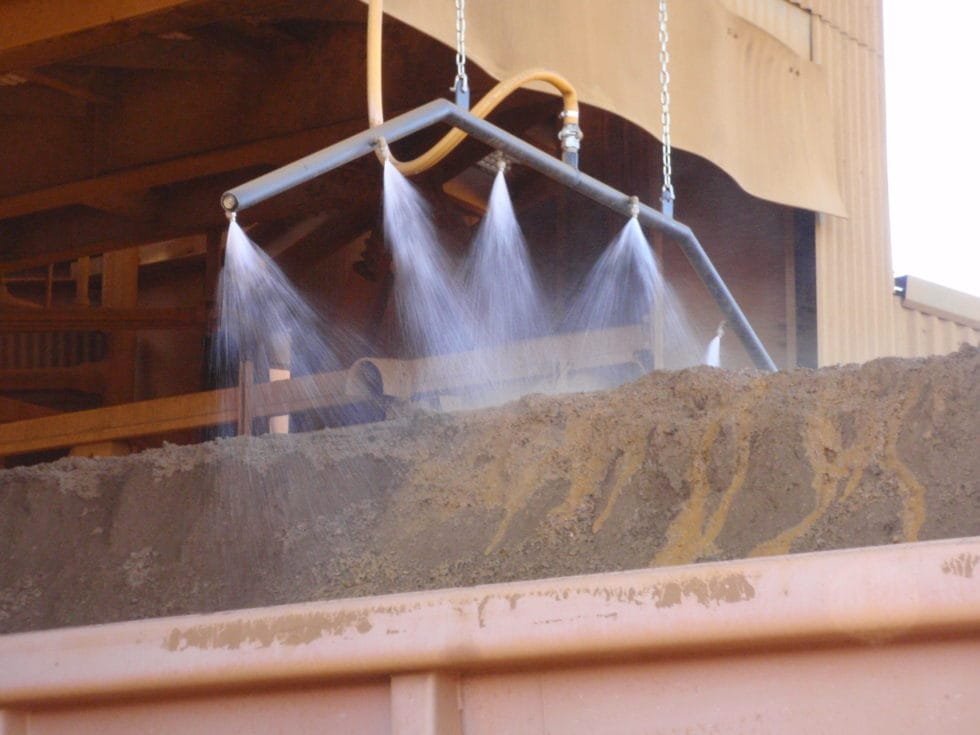 Spray header applying dust suppressant to an open rail car